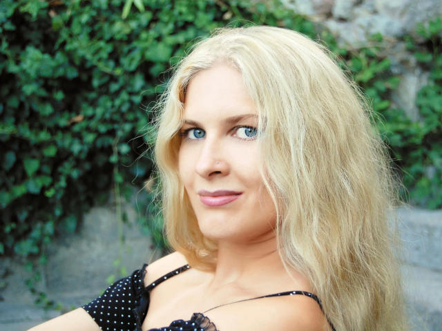 Fetish-Dreams-hot has blonde hair, blue eyes, and pink lips, wearing a black polka-dot top, with a subtle smile, showing a cute, sexy, and attractive face.