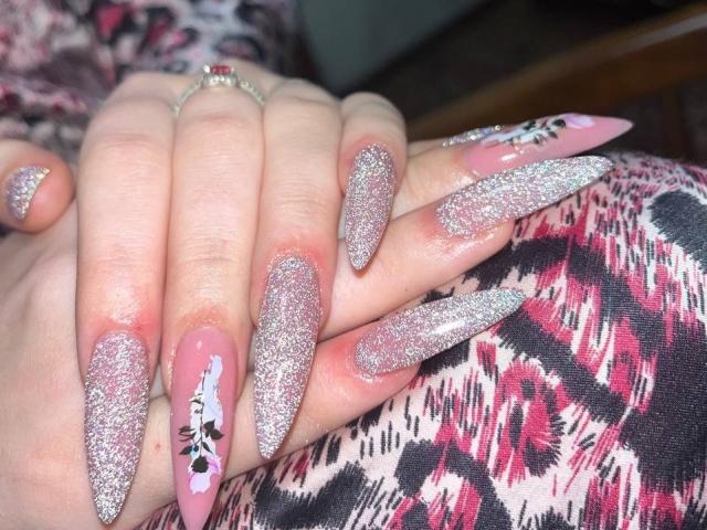 LaPulia's hands with long, glittery pink nails, one featuring a black and white floral design. Her fingers are stacked, showcasing her sparkly, pointed nails.
