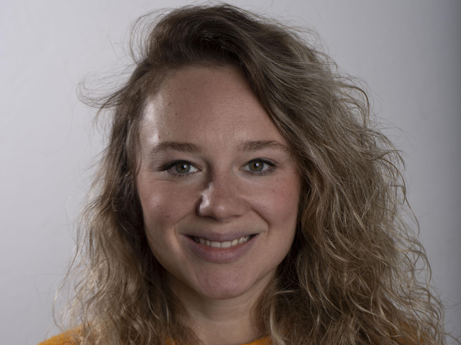 Bonnywhite hat welliges, blondes Haar, grüne Augen und ein leichtes Lächeln. Sie trägt ein gelbes Hemd, und ihre Brüste sind nicht sichtbar. Sie sieht süß und entspannt aus..
