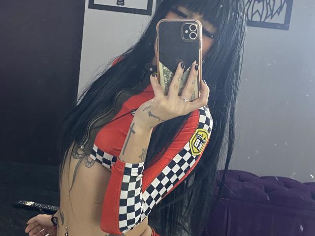 SamanthaAdele with long black hair, wearing a red and black checkered long-sleeve top, holding a phone covering her face, showing her tattoos and small tits. Mirror selfie.
