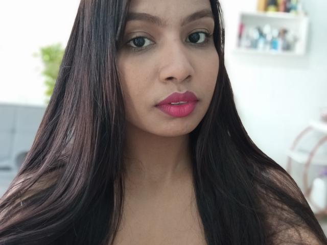 Giuliabe with long dark brown hair, light brown skin, green eyes, and pink lipstick, showing a neutral expression. Boobs not visible, focus on face.