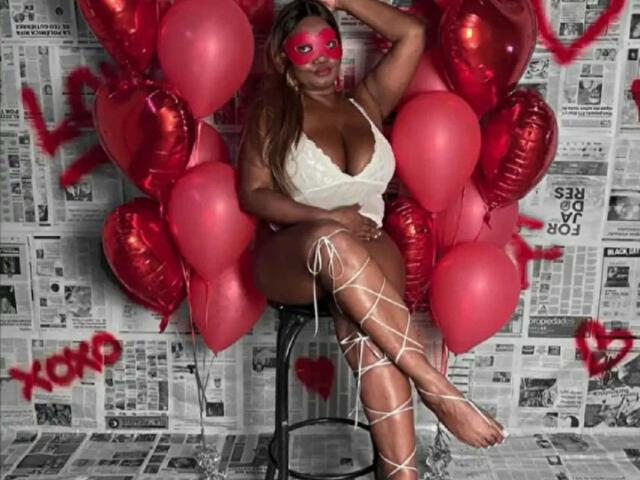 SweetBusty with big tits, red mask, white lace top, and white crisscross leg bindings, sitting on stool, surrounded by red heart balloons, in a newspaper-themed setting.