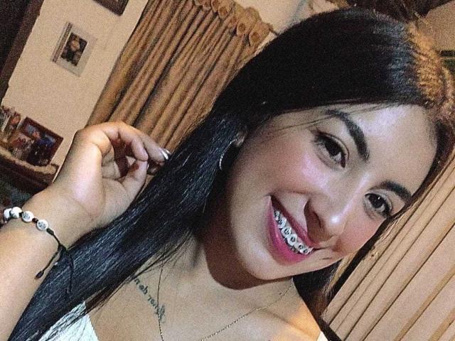 TifanyTobon with long black hair, brown eyes, and a big smile showing white teeth, has her hand in her hair, wearing a white top, and a bead bracelet.