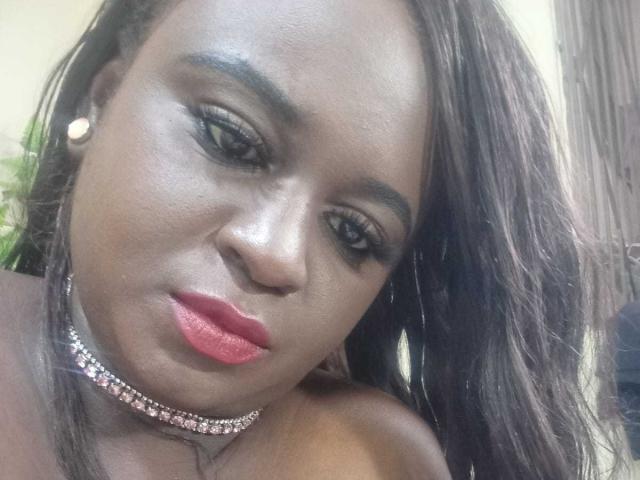 AgataYailin with dark skin, red lipstick, and a sparkling choker, looking down with half-closed eyes, wearing hoop earrings, and having long, straight brown hair.