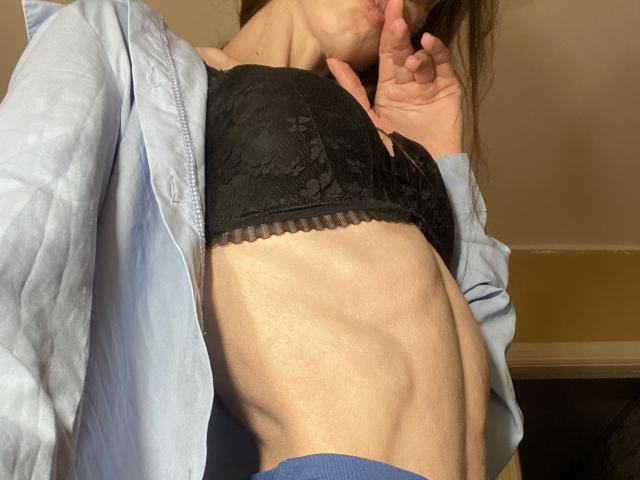 Los pechos de Kabblasha en un sujetador negro de encaje, vistiendo una camisa azul abierta, mostrando sus abdominales delgados, musculosos y definidos, con una mano cerca de su boca..