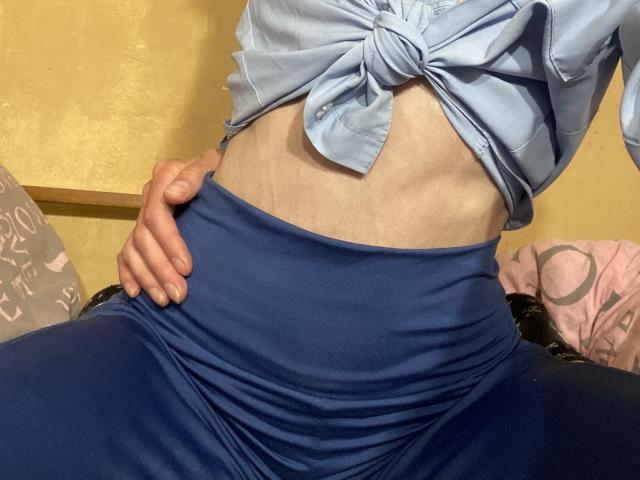 Kabblashas flacher Bauch, das blaue Hemd, das sie trägt, und ihre Hand auf der hoch taillierten blauen Hose, die einen leichten Bauchnabel zeigt. Ihre Haut ist hell. Der Fokus liegt auf ihrem Bauchbereich..