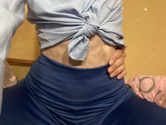 La parte centrale del corpo di Kabblasha, che mostra una camicia azzurra annodata e pantaloni blu a vita alta, con la mano destra di Kabblasha appoggiata al fianco. Addominali visibili..