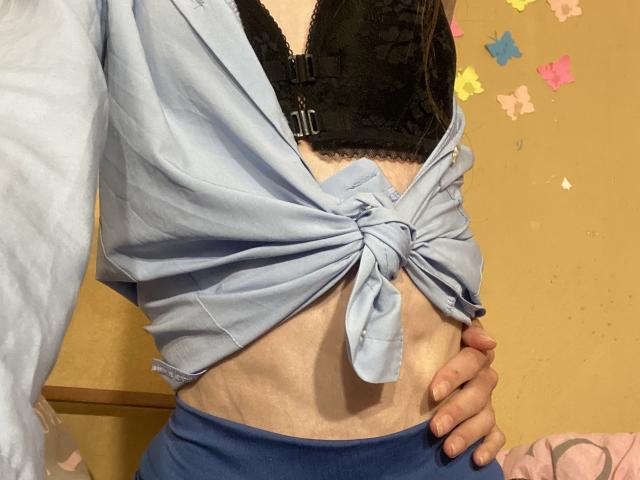 La camicia azzurra di Kabblasha era annodata davanti, rivelando un reggiseno nero in pizzo e un ventre piatto e chiaro. La sua mano poggiava sui pantaloni azzurri, mettendo in risalto una vita sottile..