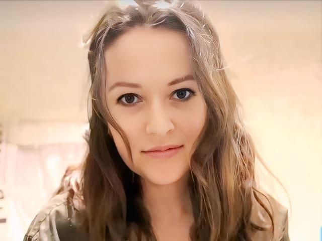 BellLizzie has wavy brown hair, blue eyes, and a slight smile. She's wearing a brown jacket, and her soft skin looks slightly flushed. Her tits are small.