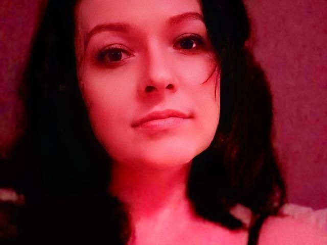 BellLizzie has pink-hued skin, dark curly hair, and a neutral expression. Her small nose and slightly parted lips are prominent. She's wearing a black top with white stripes.