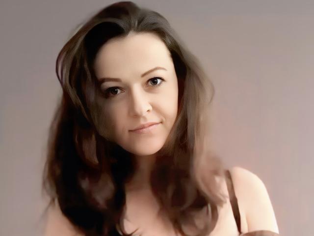 BellLizzie has wavy brown hair, light skin, and brown eyes. She's smiling slightly with a subtle nose and small lips. She's wearing a black strap.