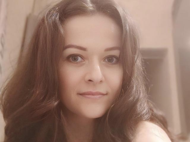 BellLizzie has brown wavy hair, light skin, and a subtle smile, with her brown eyes looking forward. Her tits are not visible, and she's wearing a strapless top.