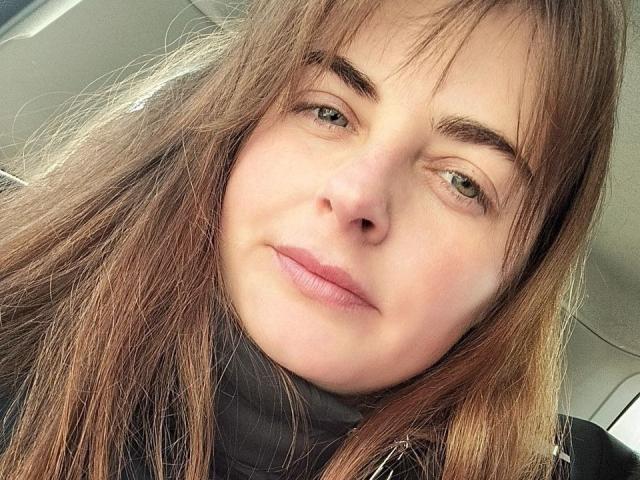 El rostro de Angela Winter, con ojos verde claro, cejas marrones y labios rosados ligeramente entreabiertos. Tiene el cabello largo y castaño, y lleva un jersey de cuello alto negro..
