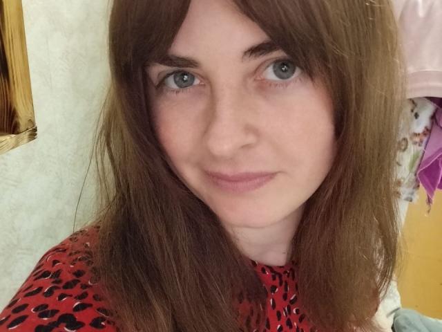Angela Winter tiene piel clara, ojos verdes y cabello castaño. Lleva un vestido rojo con lunares negros, está sonriendo ligeramente y mirando directamente a la cámara..
