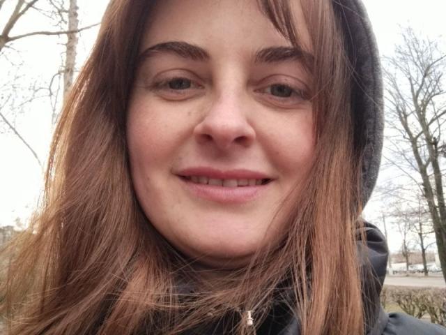 Angela Winter a les cheveux châtain clair, une capuche noire et un sourire discret qui révèle ses dents. Son nez est légèrement retroussé, et elle a de petits sourcils marron..