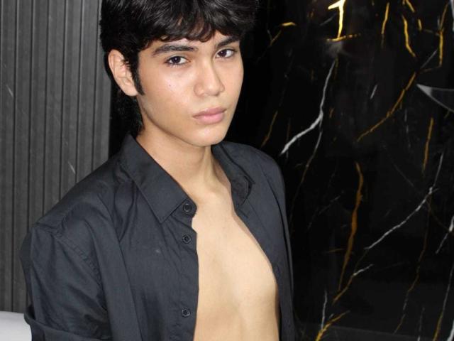 MarcoMiranda with dark hair, medium skin, and a serious expression, shirt unbuttoned to reveal his bare chest, in a black, slightly shiny shirt.