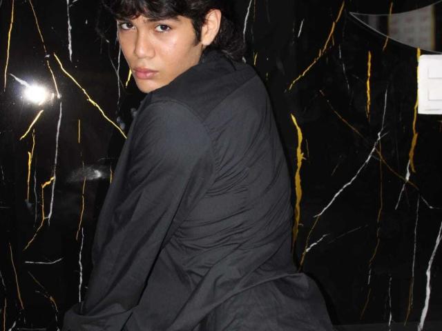 MarcoMiranda with dark curly hair, wearing a black shirt, looking over shoulder, black marble background with gold and white veins, slightly glossy, seductive, attractive, slim build.
