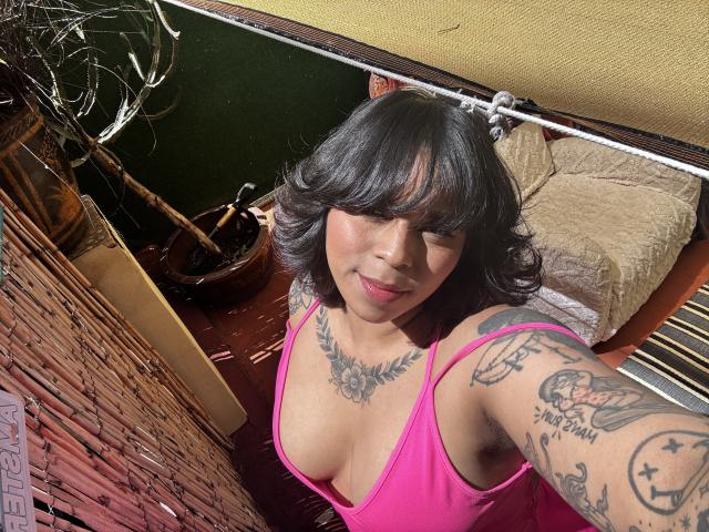 Chili, con i capelli neri e tatuaggi, in top rosa, sorridente, seni medi, selfie, luce del sole, cuscino giallo, sfondo di cracked.