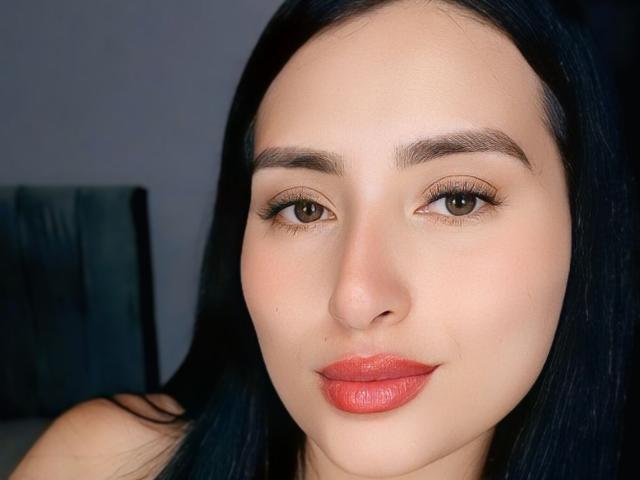 VaneHot69 a un visage mignon avec une peau claire, des yeux marron foncé, de longs cheveux noirs et du rouge à lèvres rose. Ses sourcils sont épais et elle regarde directement l'appareil photo..