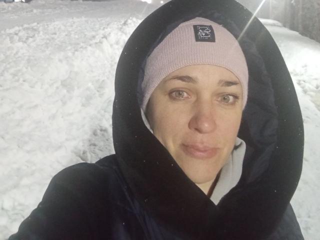 MuseOfSelene with a pink headband, black hoodie, and no makeup, showing a neutral expression, in a snowy setting. Her ass is not visible. Snow and light in background.
