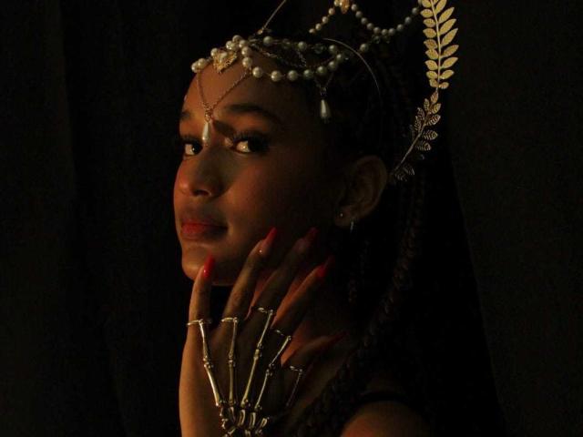 Ally Mills met donkere huid, rode nagels en gouden sieraden, draagt een parelhoofddeksel, kijkt opzij, handen in de buurt van het gezicht, donkere achtergrond, zachte belichting, elegant, sexy..