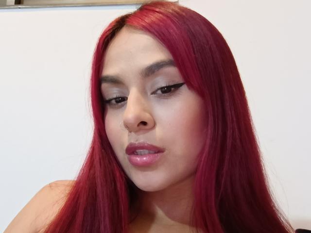 EmilyEvanss has red hair, a nose ring, and is looking down with black eyeliner and pink glossy lips. Her ass is not visible.