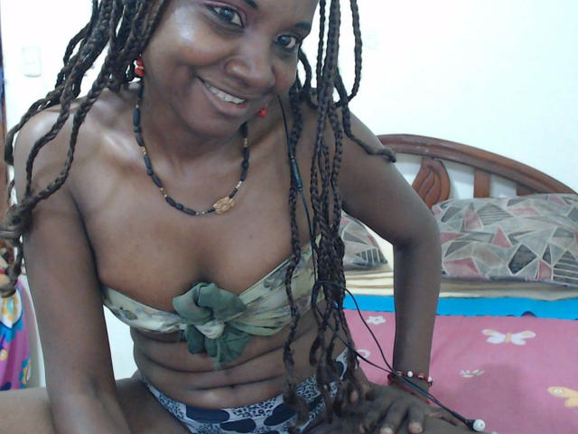 Katrhina87-hot, dark-skinned with long braids, smiling, wearing a camo bikini top with green bow, showing her tits, wearing leopard-print panties, on a bed.