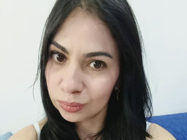 SaraLunaBella69 with puffy red lips, dark brown eyes, and black hair, wearing a white tank top, looking slightly annoyed. Boobs not visible, ass not visible.