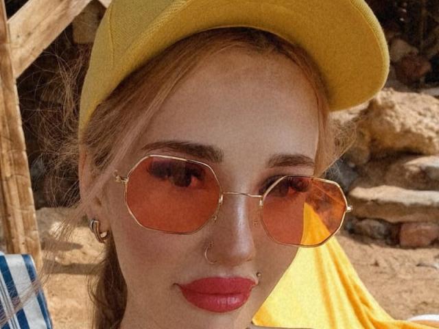 AlienNina with yellow hat, red lips, nose ring, septum ring, and gold aviator sunglasses, showing off her hot face and cute butt-reflecting glasses.