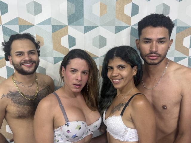 Four people, BebeTransAndTwoGuy, in a photo. TwoGuy with curly hair, chest tattoos, gold chain, and hairy chest. TwoBebe with large tits, white bra, and tattoo. TwoGuy with short hair, necklace.