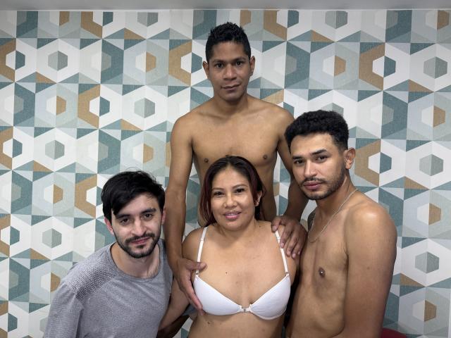 Vier Personen, SamyraSexGroupBest steht mitten drin ohne Hemd, mit den Händen auf den Schultern, SamyraSexGroupBest trägt einen weißen BH, zwei SamyraSexGroupBests mit kurzen, lockigen Haaren, eine davon trägt ein graues Hemd..