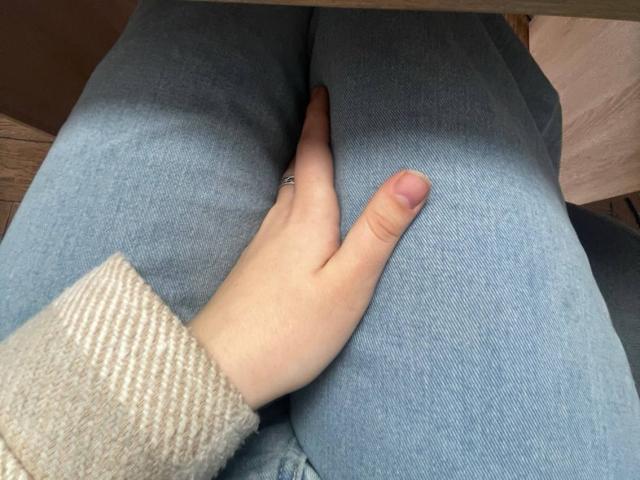 LaPulia's hand with a ring on the index finger rests on her blue jeans, showing her pale skin and beige knitted sleeve. Her fingers are gently pressing her ass.