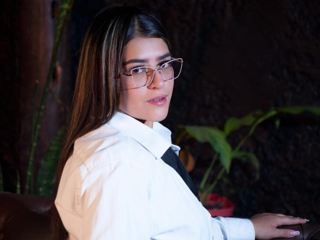 NicoleAcosta with long brown hair, wearing glasses and a white shirt, looking over her shoulder with a slight smile, showing her pouty lips and cute ass.