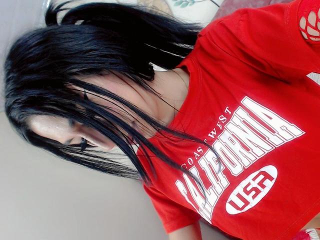 Kendalla, con cabello negro, una camisa roja y los senos visibles, mirando hacia abajo con el cabello cubriendo su rostro, vistiendo un logo blanco que dice "USA". Es linda, y su cabello está despeinado..