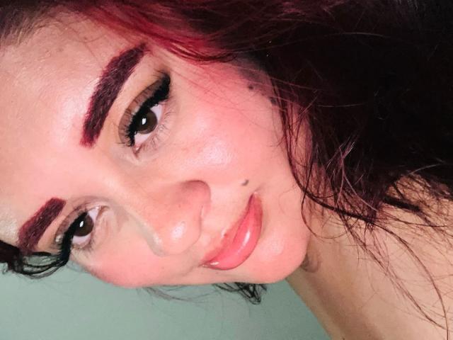 DaniielaaCorrtazaar has red eyebrows, black eyeliner, glossy pink lips, and a small mole on her nose. Her pinkish skin and wet dark hair are visible in the selfie.