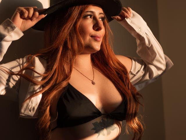 AnniaLeRoux with long red hair, black hat, white shirt, and black bikini top, hands on hat, tattoo on her right side, necklace, sunlight, soft smile, sexy, confident.