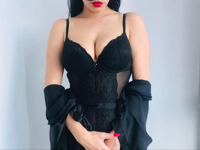 AdrianaLeone-hot with black lace lingerie, showing off her tits, wearing a black robe off her shoulders, red lipstick, and black nails, against a white background.