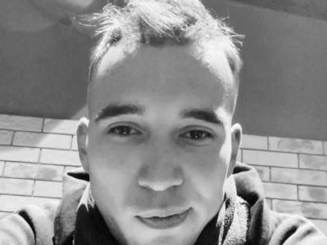EmmettSmile's face, short messy hair, slight smile, wearing a hoodie, black and white selfie, visible nose and eyes, slight shadow on the left side, medium skin tone.