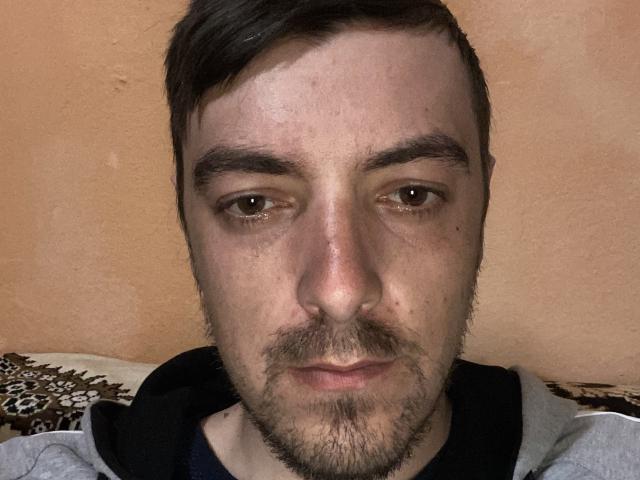 MaxenRace has a slightly sweaty, serious face with brown eyes, dark eyebrows, short brown hair, a light beard, and a gray hoodie. His nose is centered in the frame.