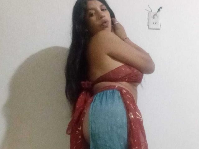 LizzyThompson with long black hair, wearing a red and blue wrap dress, showing her back and ass, looking over her shoulder with a slight pout.