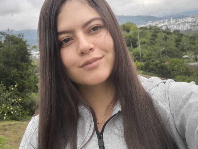 Sukilove has long brown hair, light brown eyes, and a slight smile. She's wearing a gray hoodie, with a calm, confident expression. Her ass is not visible.