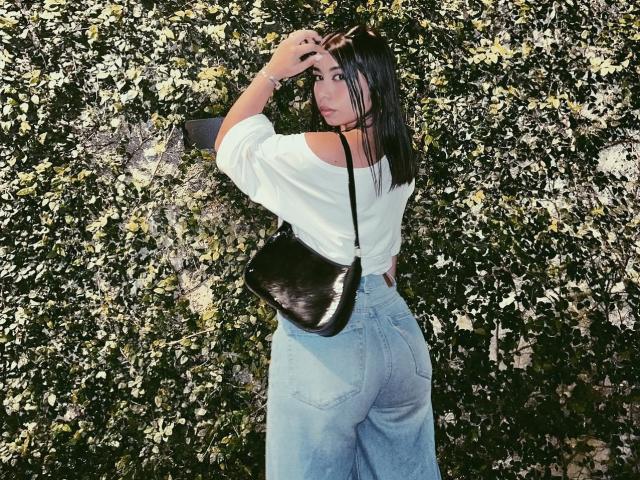 Lananexdoor15 with black shoulder bag, white off-shoulder top, and high-waisted blue jeans, showing her ass, looking over shoulder with hand in hair.