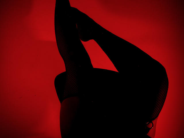 AdaMclain's black fishnet-covered legs and butt are raised in a sexy pose, with a red background. Her foot is pointed up, showing off her flexible, sexy form.