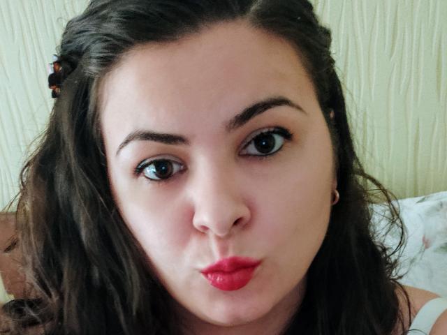KathyKrystal has pouty red lips, dark wavy hair, and is making a puffy face with her eyes looking slightly to the side. She's wearing small hoop earrings.
