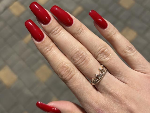 Karish's hand with shiny red nails, a gold ring with small jewels, and pale skin. The nails are long and glossy, contrasting with the ring's intricate design.