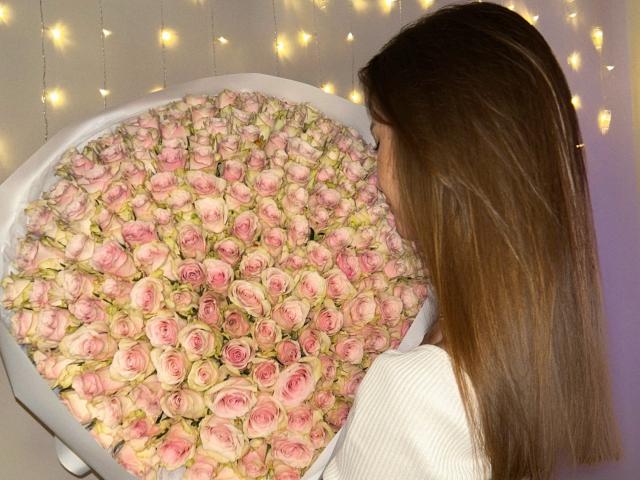 Karish with long brown hair, white top, facing large bouquet of pink roses, staring at them, surrounded by warm fairy lights.