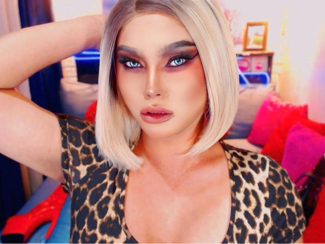 QueenNhicolle-hot with blonde bob, wearing leopard print top, has blue eyes, dark eyeliner, and pink lipstick, hand in hair, looking at camera with a slight pout.