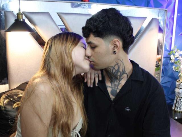 BelialAndLilim with long brown hair, kissing BelialAndLilim with dark curly hair, black shirt, and tattoo on neck. BelialAndLilim's hand on BelialAndLilim's chest. Soft light.