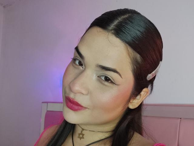 AntonelaPark has dark hair in a side part, pink lipstick, and a star necklace, with a hairclip on the right. She's smiling with arched eyebrows.