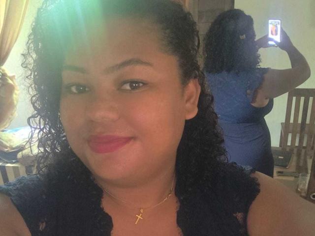 WendyStar69 with curly black hair, red lipstick, and a blue lace dress, smiling at the camera, while taking a mirror selfie showing her back and ass.